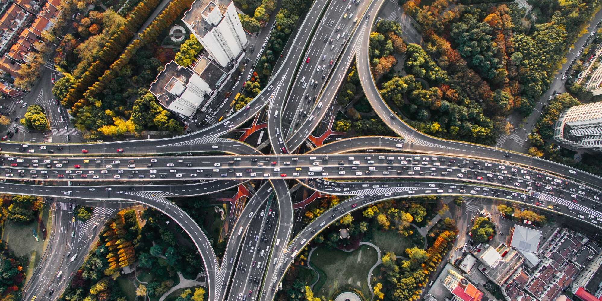 People-Process-Change-Strategy-Planning-min Aerial view of a complex highway interchange amidst greenery and urban buildings.