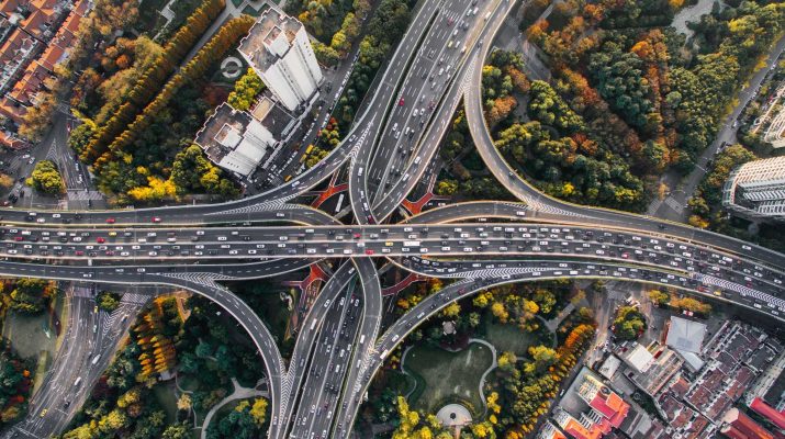 Aerial view of a complex highway interchange amidst greenery and urban buildings.