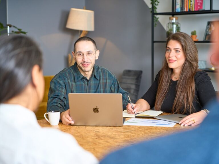 Team members at a table with laptops, a man smiling, engaging in discussion.